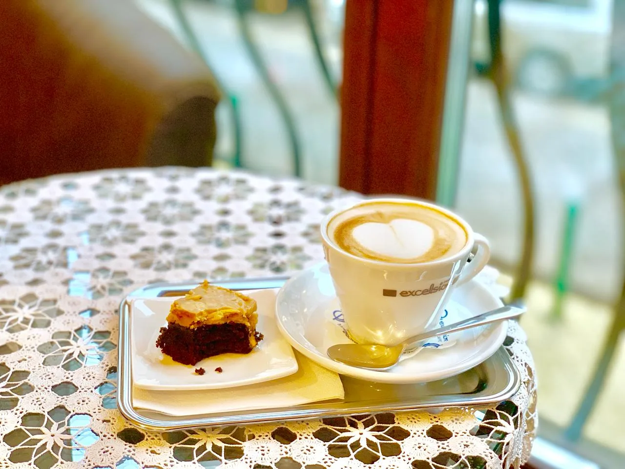Cappuccino with a heart in the milk foam and a slice of chocolate cake on a lace-covered table